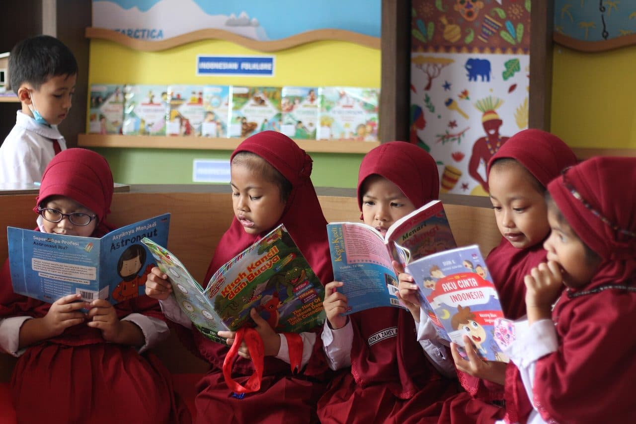 Sekelompok siswa sekolah dasar berseragam merah membaca buku bersama di perpustakaan sekolah